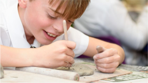 Smiling young boy in a white shirt engaging in a clay modeling activity.